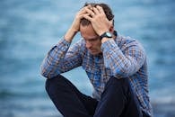 pexels-photo-897817-897817 A man in a plaid shirt sits by the water looking distressed, symbolizing stress.
